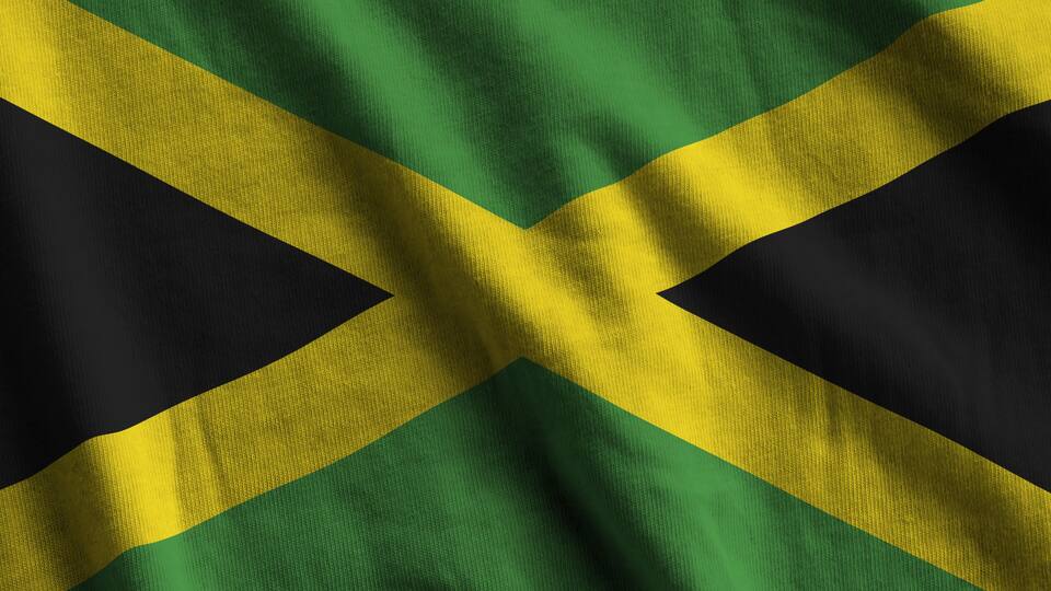 Jamaica flag with big folds waving close up under the studio light indoors. The official symbols and colors in fabric banner