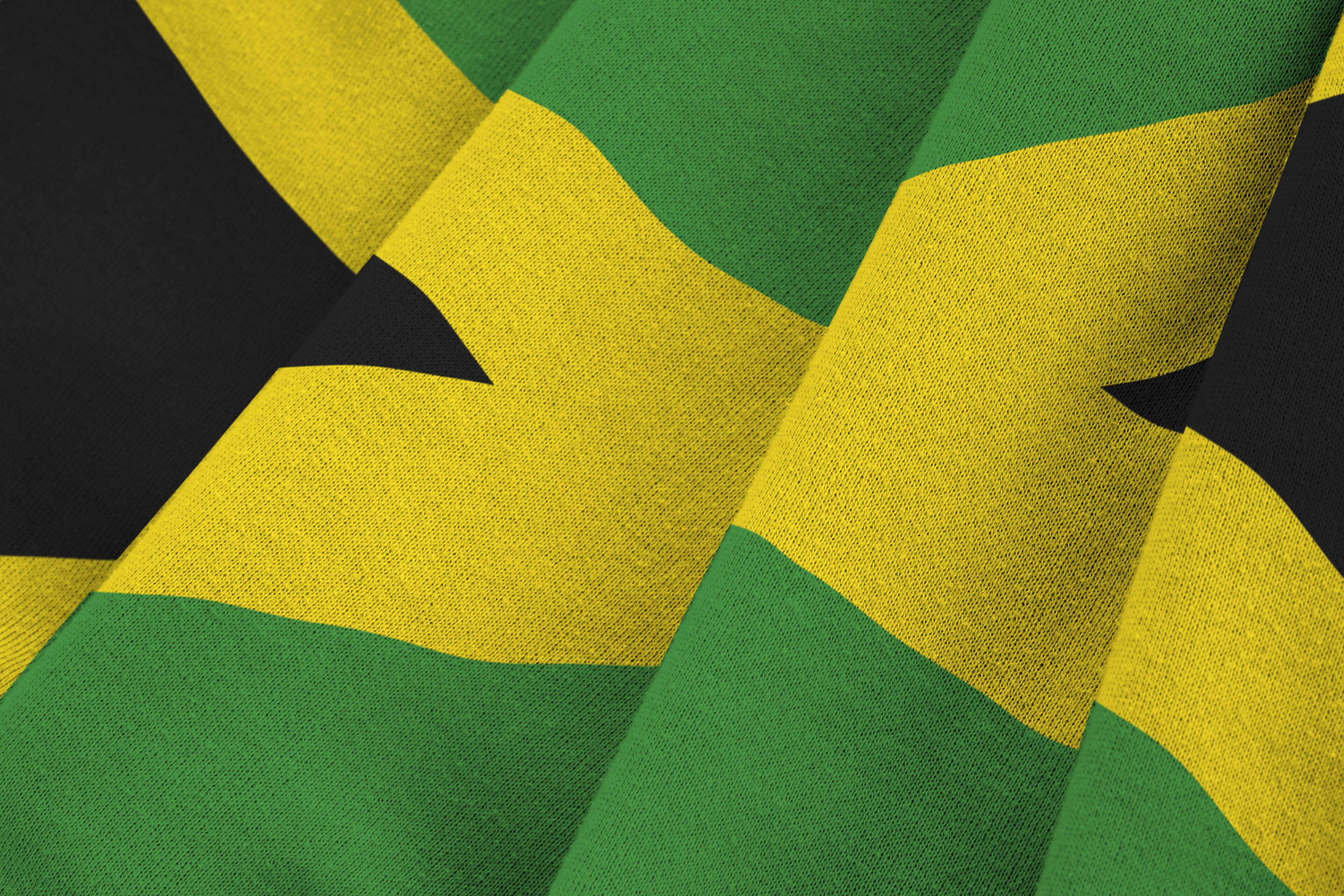Jamaica flag with big folds waving close up under the studio light indoors. The official symbols and colors in fabric banner