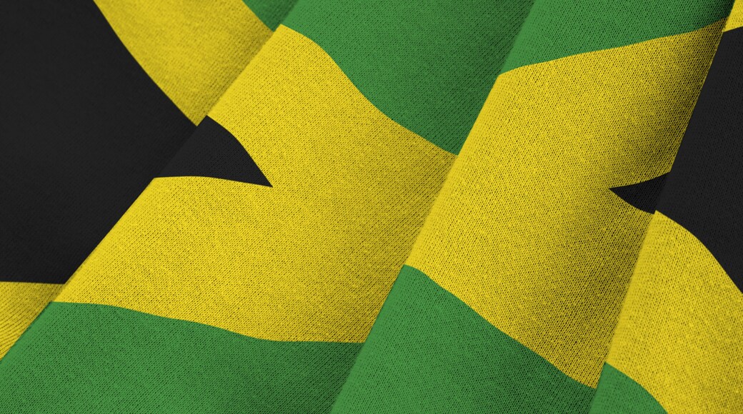 Jamaica flag with big folds waving close up under the studio light indoors. The official symbols and colors in fabric banner