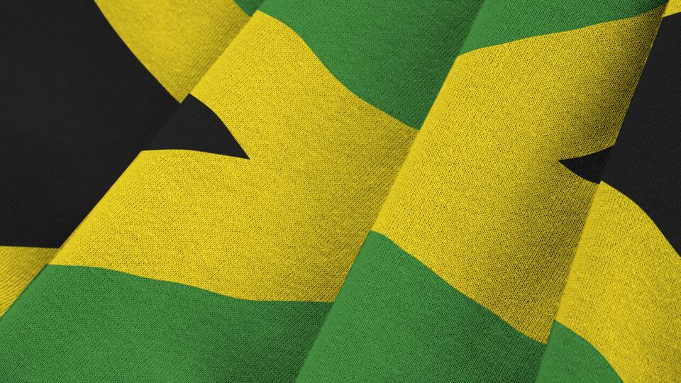 Jamaica flag with big folds waving close up under the studio light indoors. The official symbols and colors in fabric banner