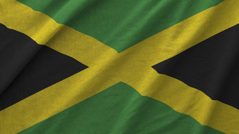 Jamaica flag depicted on folded wavy fabric of old cloth close up
