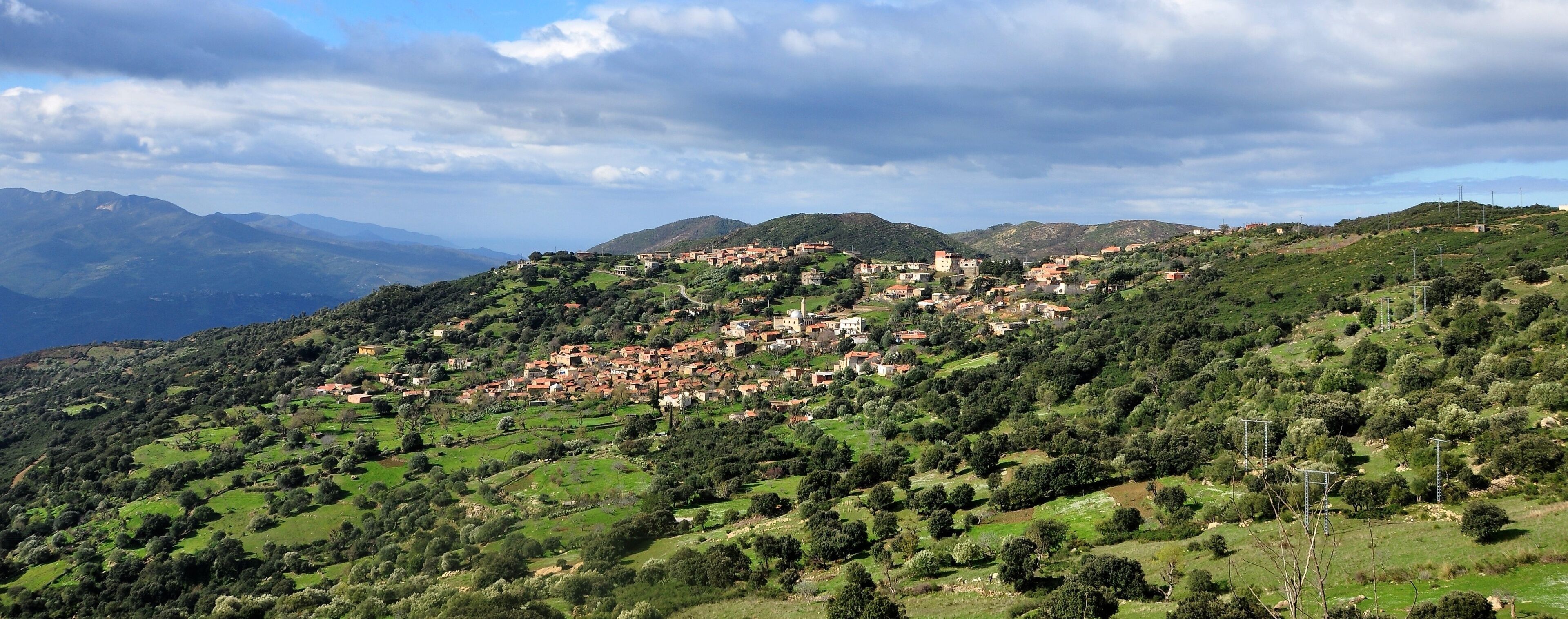 A hillside village with buildings nestled among green hills and mountains in the background.