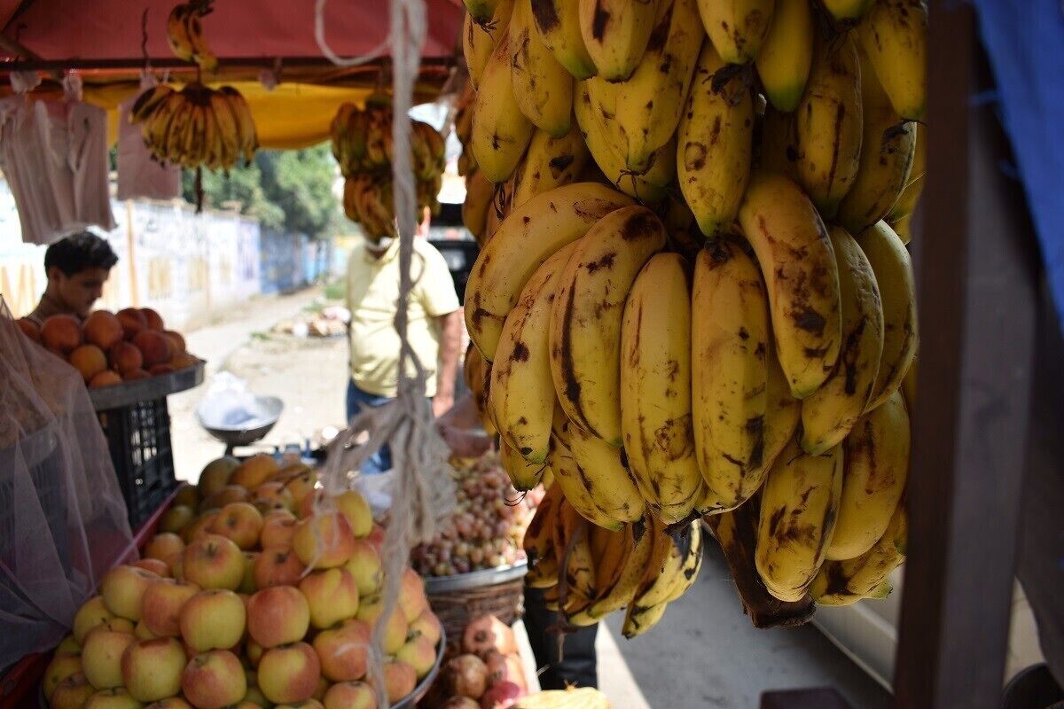 A fruit market with bananas, apples, and oranges on display.
