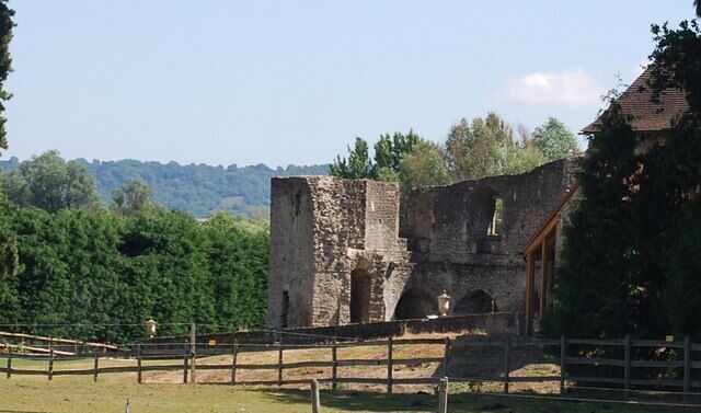 An ancient stone structure with arches, surrounded by greenery and a clear sky.