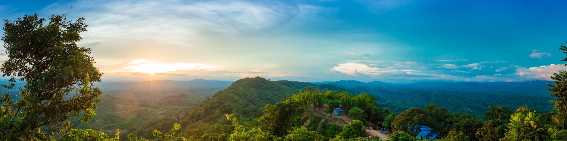 A lush green landscape with a clear sky, a sun setting or rising over a mountain range, and a small blue house in the foreground.