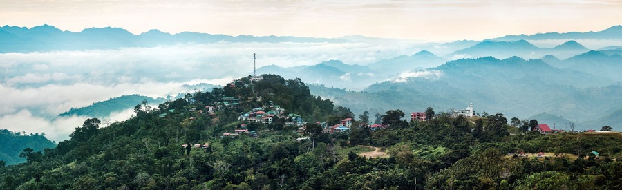 Sajek, Bangladesh - 04 December 2023: View of the undulating hills and valleys shrouded in a soft, ethereal mist, dotted with clusters of houses and structures.