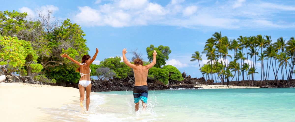 A beach with clear turquoise water, palm trees, and rocky outcrops.