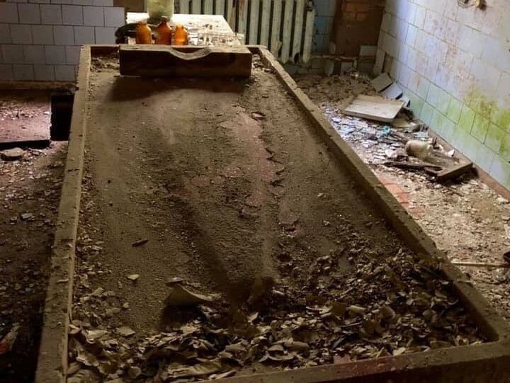 Una habitación desordenada y polvorienta con escombros dispersos y un ventanal roto.