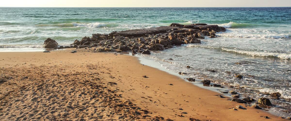 A sandy beach with scattered rocks and waves approaching the shore.