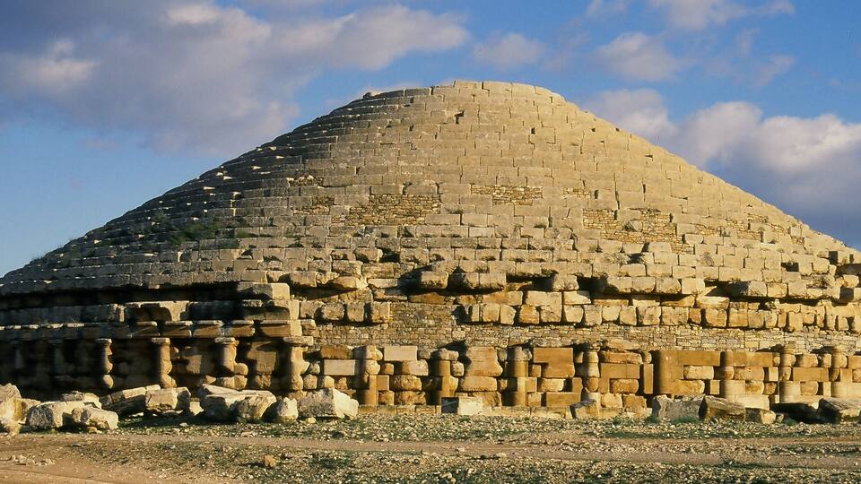 A large, ancient stone structure with a rounded top and a flat base, surrounded by scattered rocks and debris.