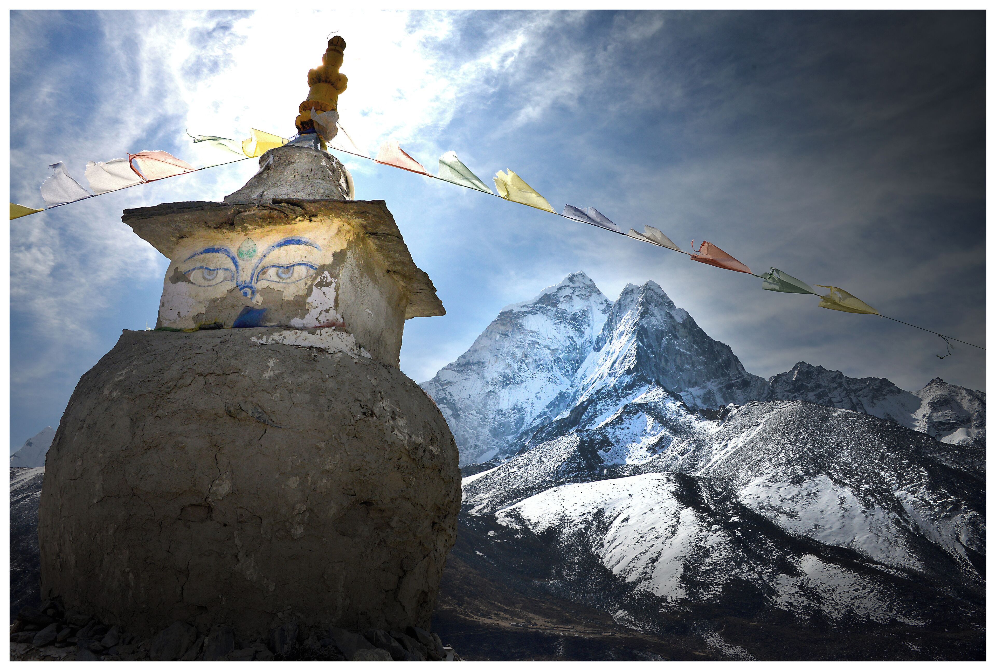 A prayer wheel with colorful prayer flags in front of snow-capped mountains.