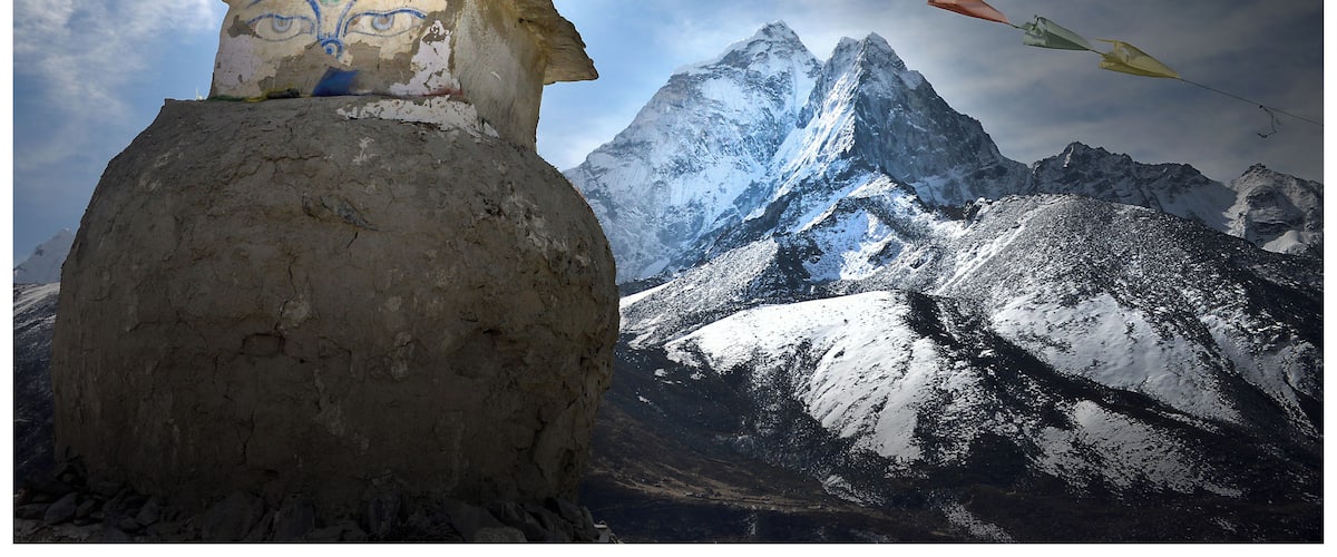 A prayer wheel with colorful prayer flags in front of snow-capped mountains.