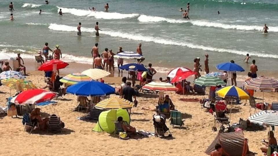 A crowded beach with people swimming and sunbathing under colorful umbrellas.