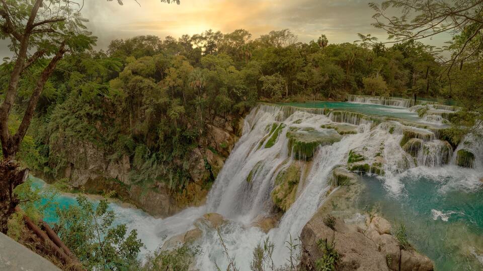 A multi-tiered waterfall surrounded by dense forest.