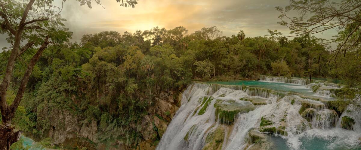 A multi-tiered waterfall surrounded by dense forest.