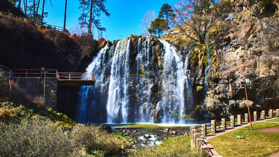 A waterfall cascading down a rocky cliff, surrounded by trees and a viewing platform.