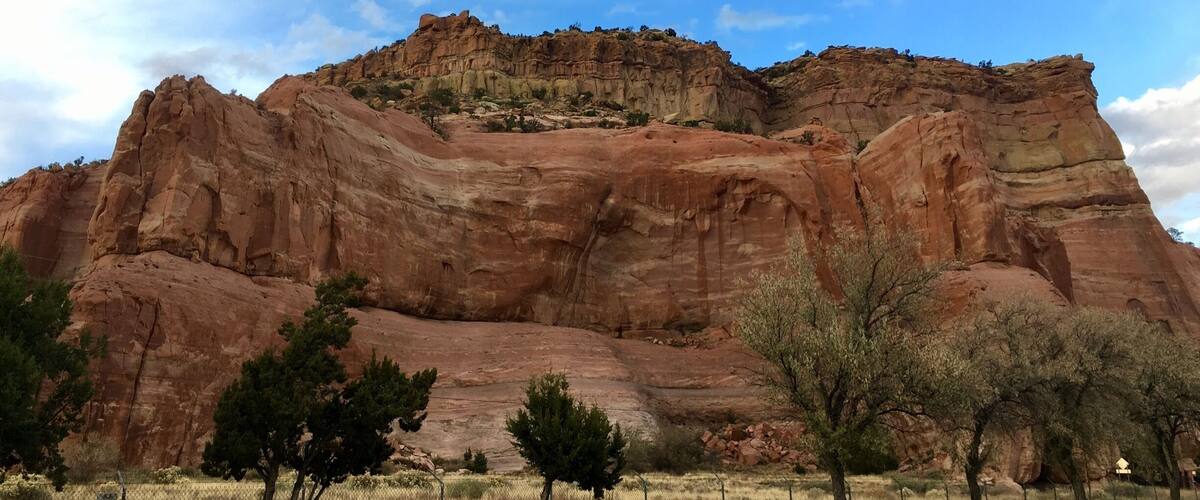 A large red rock formation with trees in the foreground.