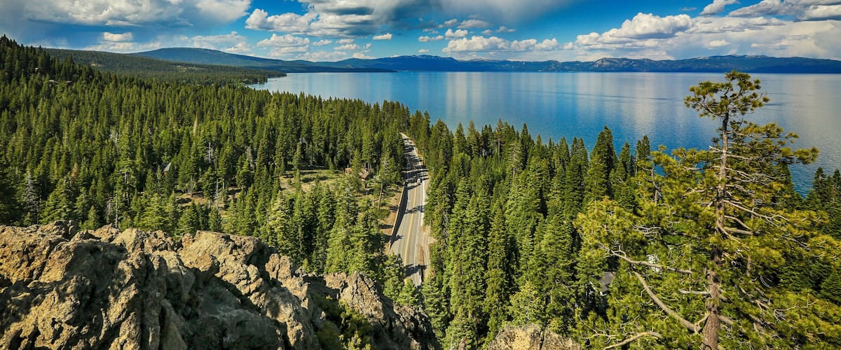 A mountainous landscape with a clear lake, dense forest, and a winding road.
