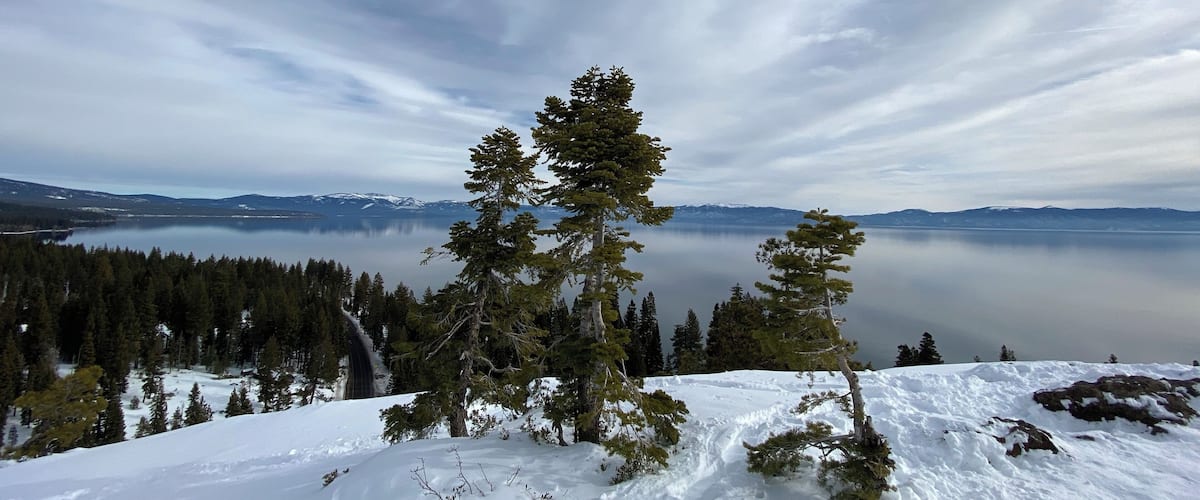Ein mit Schnee bedeckter Berg mit einem klaren See und Bergen im Hintergrund.