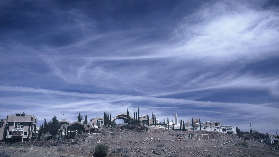 A ruined landscape with overcast skies and scattered buildings.