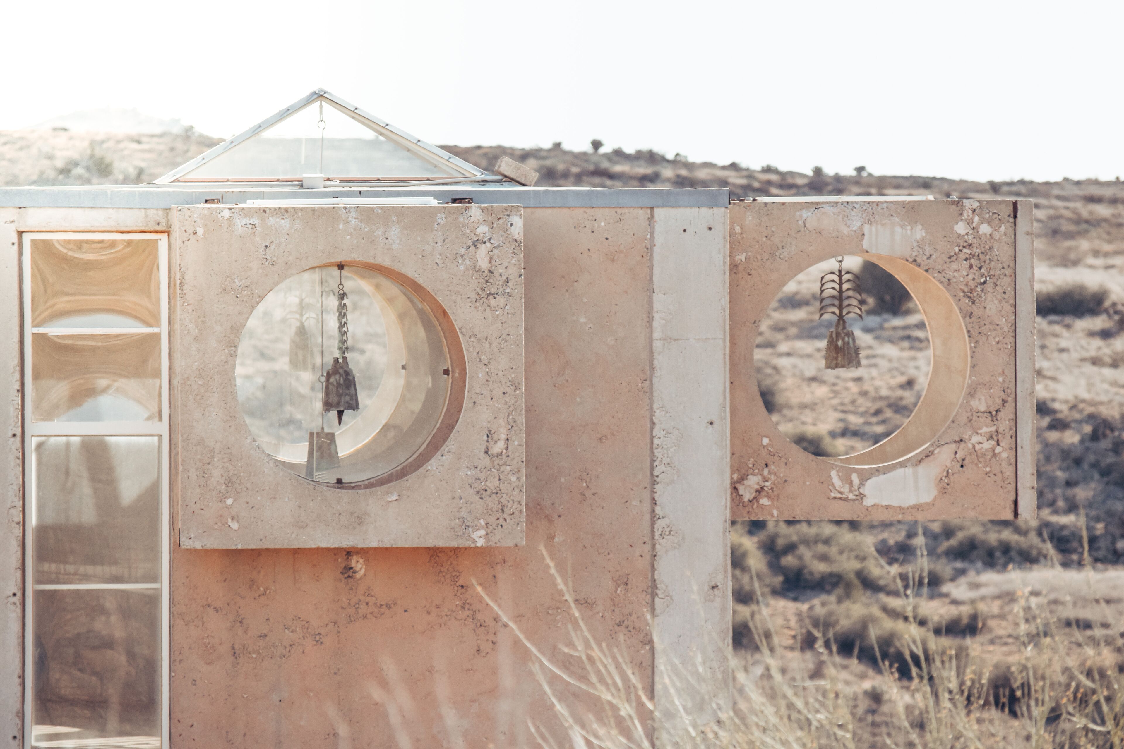 A rustic, weathered structure with circular windows and a triangular roof, set against a dry, grassy landscape.