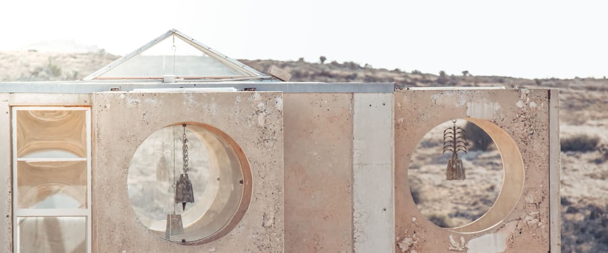 A rustic, weathered structure with circular windows and a triangular roof, set against a dry, grassy landscape.