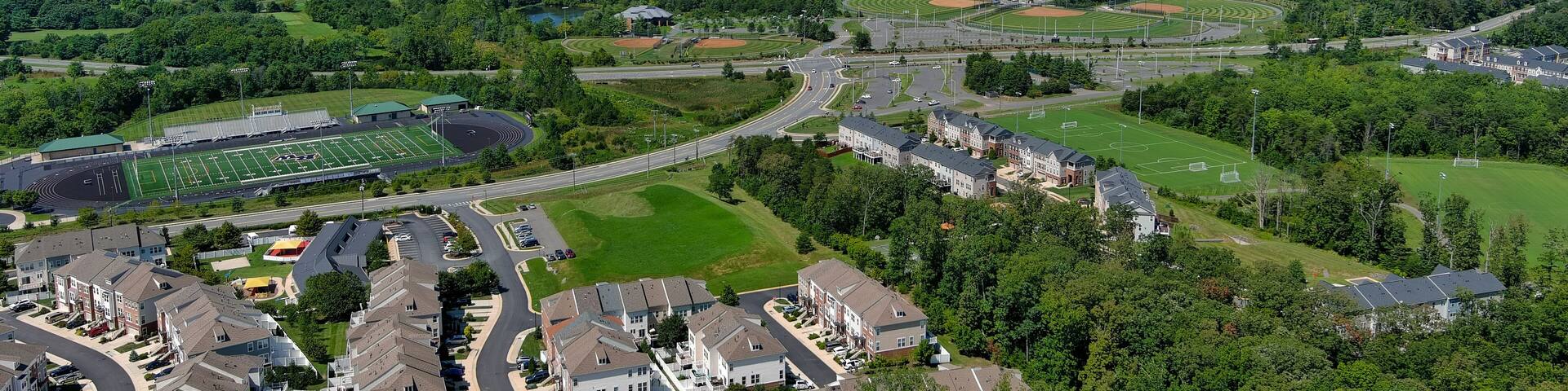 A suburban area with residential buildings, a football field, and a lake in the distance.