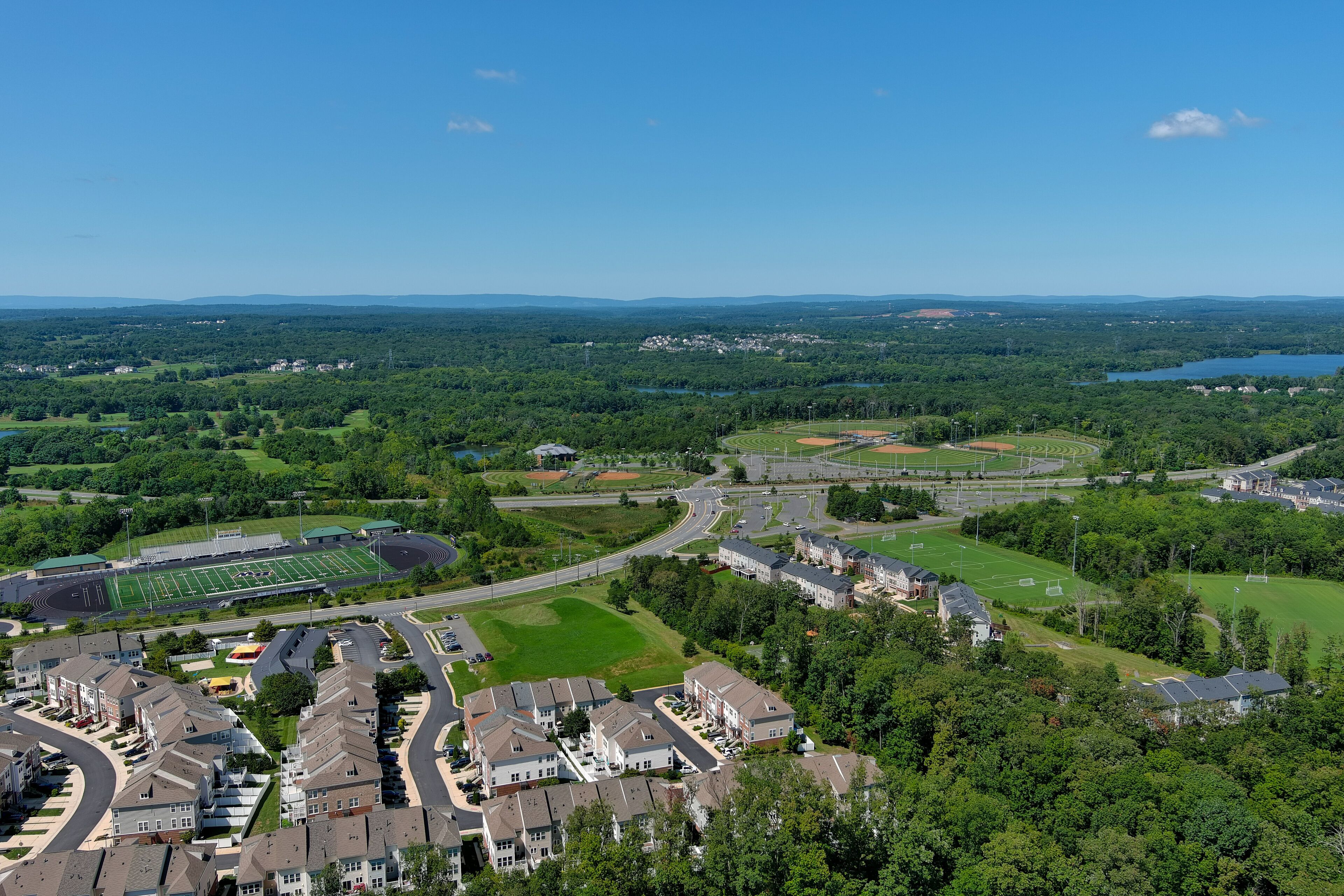 A suburban area with residential buildings, a football field, and a lake in the distance.