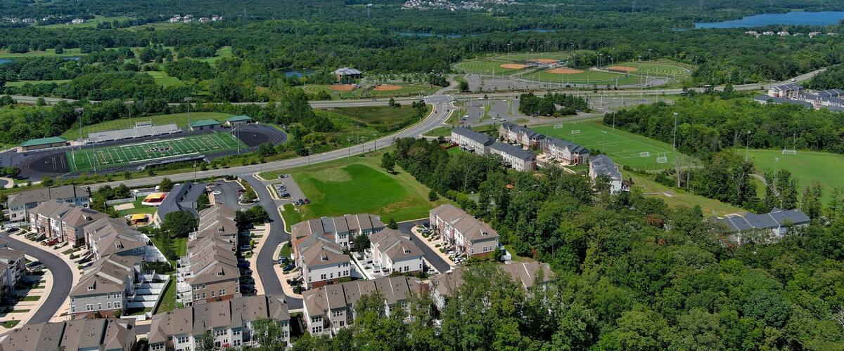 A suburban area with residential buildings, a football field, and a lake in the distance.