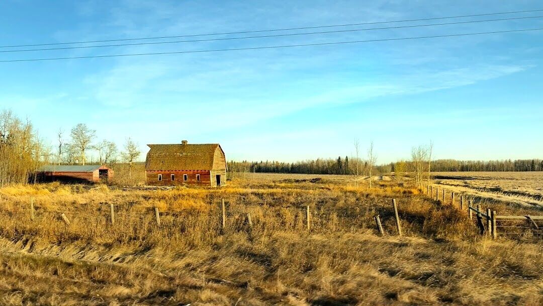 A rural landscape with a red barn, a fenced field, and a clear sky.