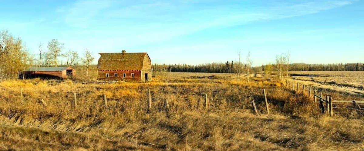 A rural landscape with a red barn, a fenced field, and a clear sky.