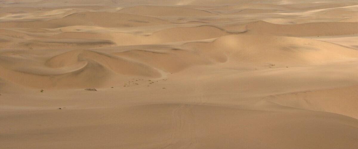 A vast desert landscape with undulating sand dunes under a cloudy sky.