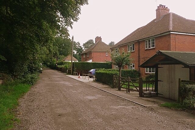 A gravel driveway in a residential area with houses, a wooden fence, and a covered bench.