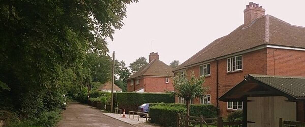 A gravel driveway in a residential area with houses, a wooden fence, and a covered bench.