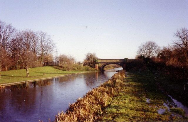 A river with a bridge, grassy banks, and leafless trees.