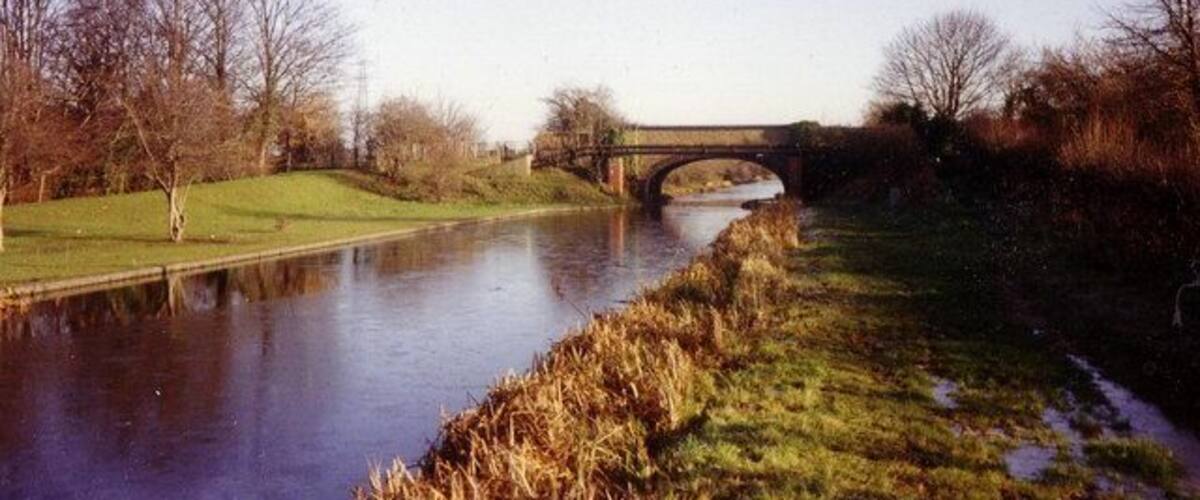 A river with a bridge, grassy banks, and leafless trees.