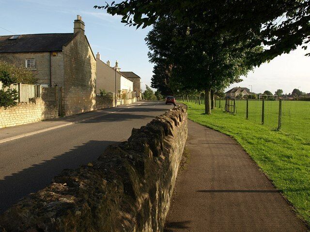 A rural road with stone walls, a sidewalk, and houses.