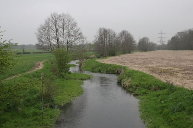 A narrow water channel in a rural landscape with trees and open fields.
