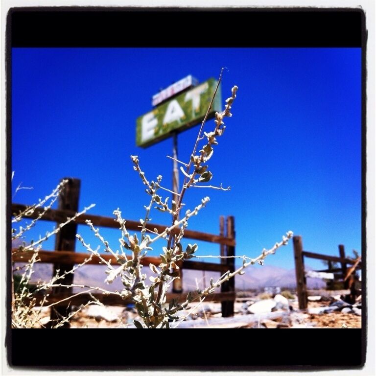 A desert landscape with a wooden fence and a sign that reads "EAT."