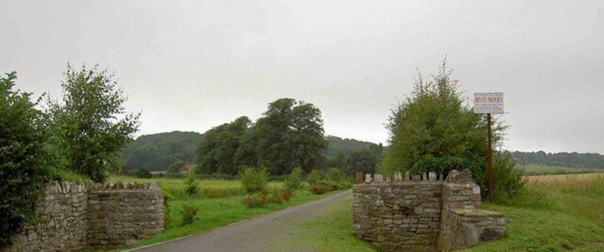 A rural road with stone walls on either side and a signpost in the distance.