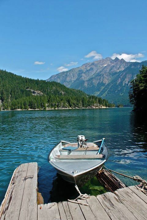 A small boat tied to a wooden dock on a calm lake with mountains in the background.