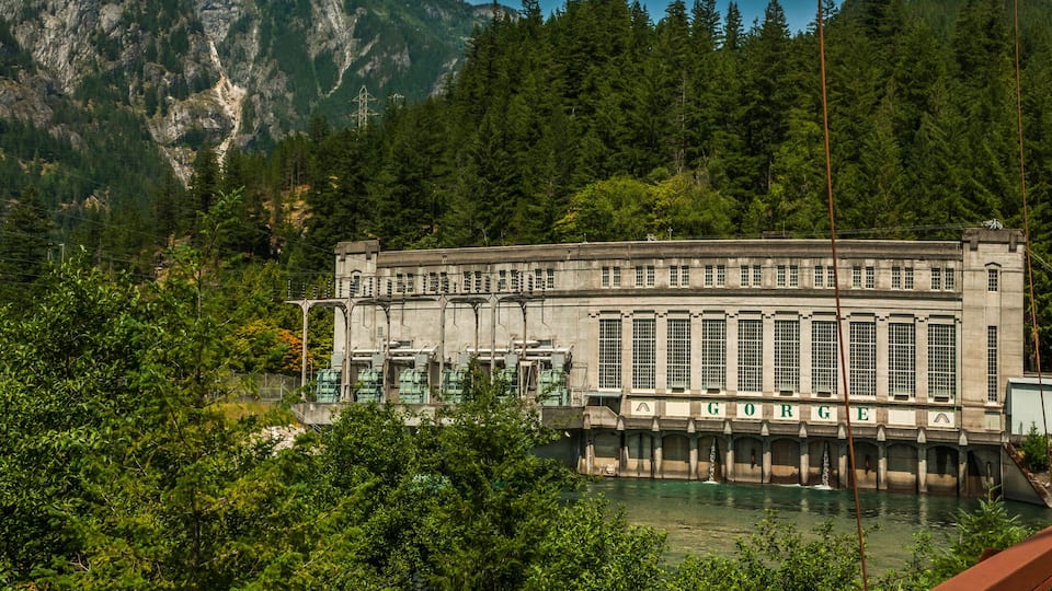 A dam with a water reservoir, surrounded by dense forest and mountains.