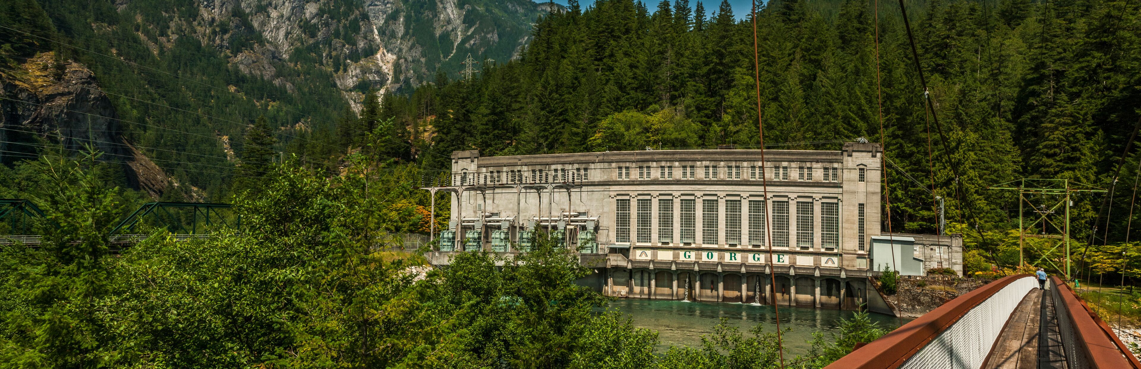 A dam with a water reservoir, surrounded by dense forest and mountains.