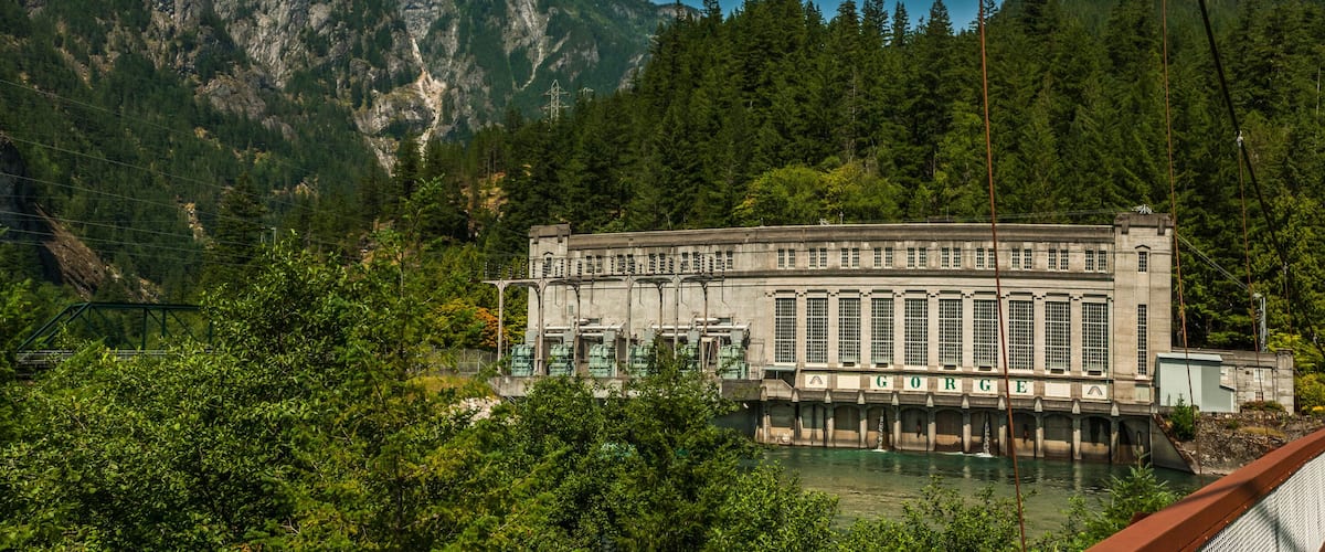 A dam with a water reservoir, surrounded by dense forest and mountains.