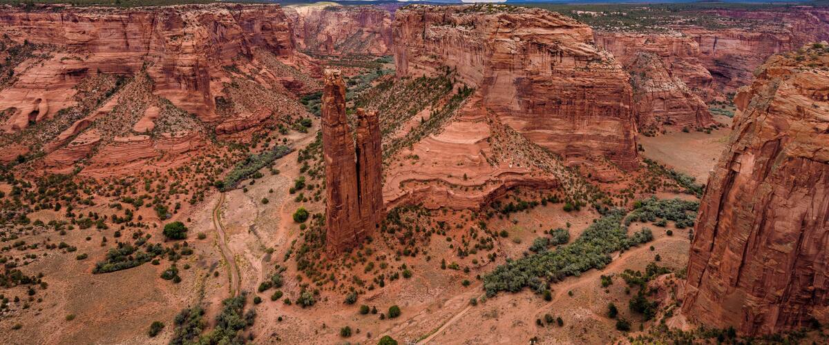 A canyon with red rock formations, green vegetation, and a cloudy sky.