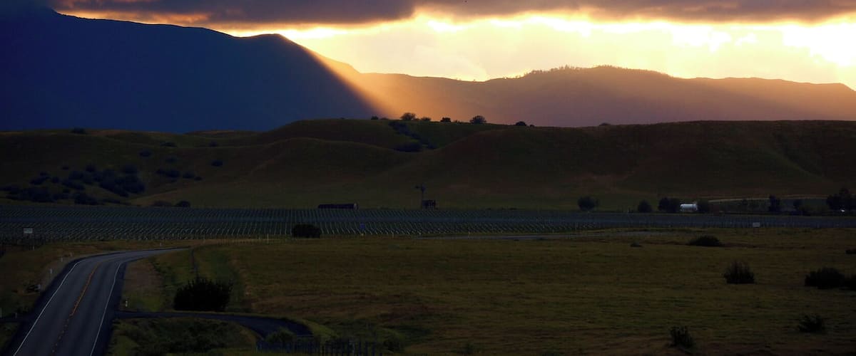 A rural landscape with rolling hills, a road, and a solar farm.