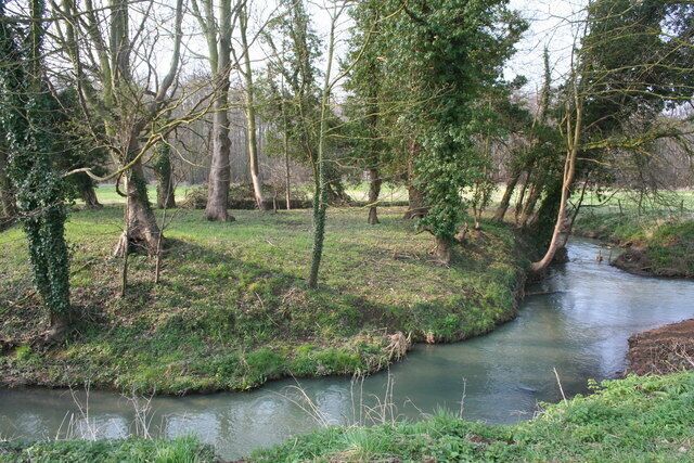 A calm river winding through a wooded area with trees and grassy banks.