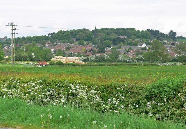 A rural landscape with fields, hay bales, and a village in the background.