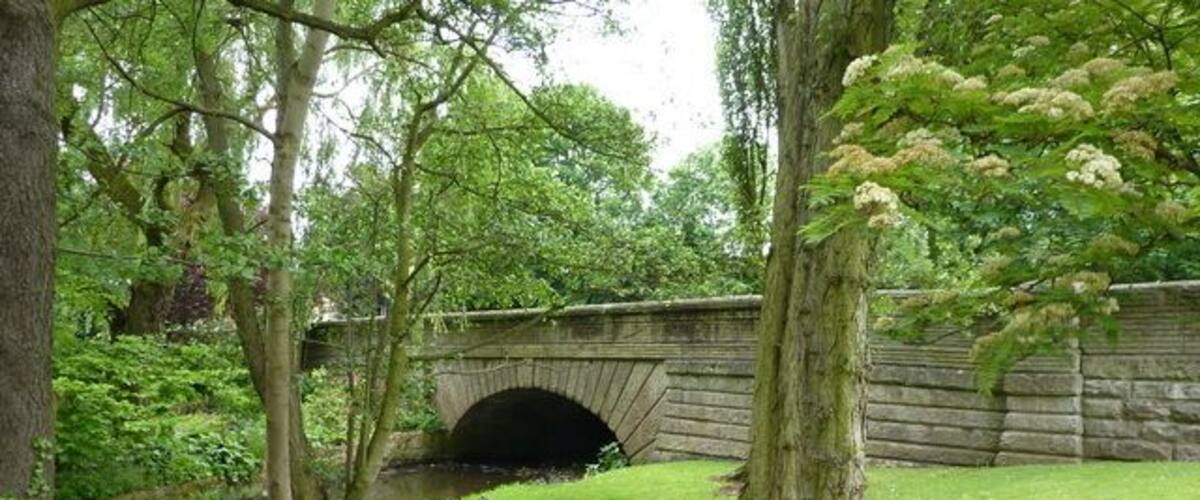 A stone bridge over a river, surrounded by lush greenery and trees.