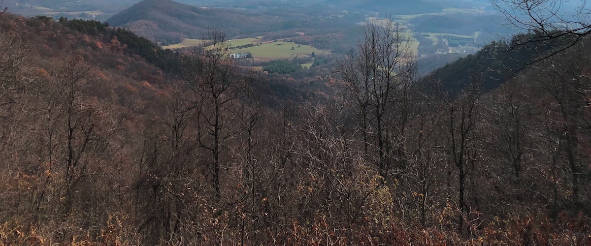 A mountainous landscape with autumn foliage, distant valleys, and a partly cloudy sky.